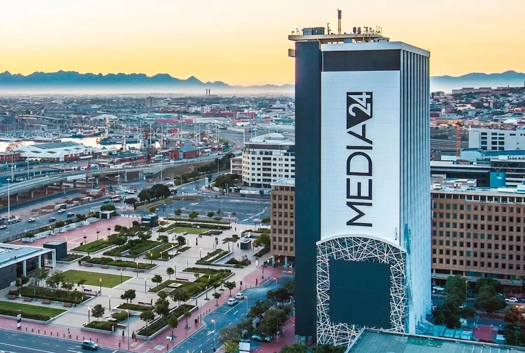 Tall Media24 building with large black text on a white facade, situated in an urban city plaza.